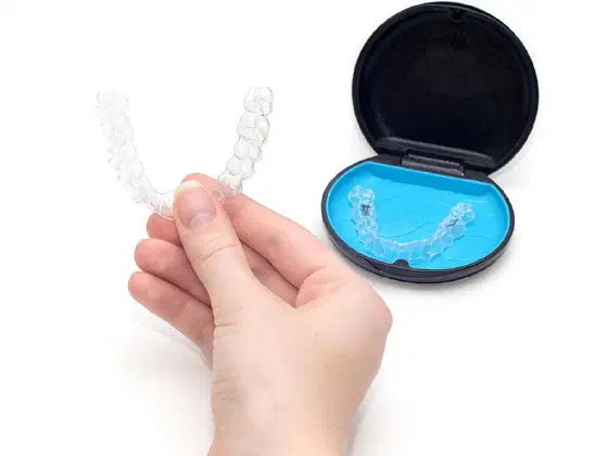 Hand holding a clear Invisalign aligner next to its case